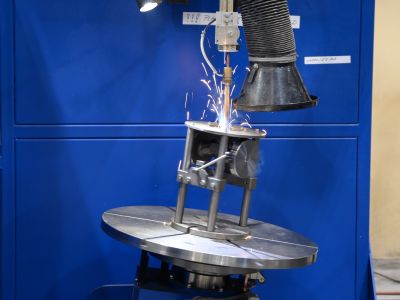 Industrielle Produktionsanlage mit Ventil unter einer Schwei&szlig;vorrichtung und Inspektionslicht vor blauem Hintergrund. | Copyright: PROVALVE Armaturen GmbH & Co. KG